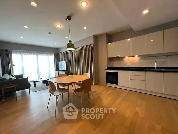 Spacious modern living room with open kitchen and dining area, featuring sleek cabinetry and natural light.