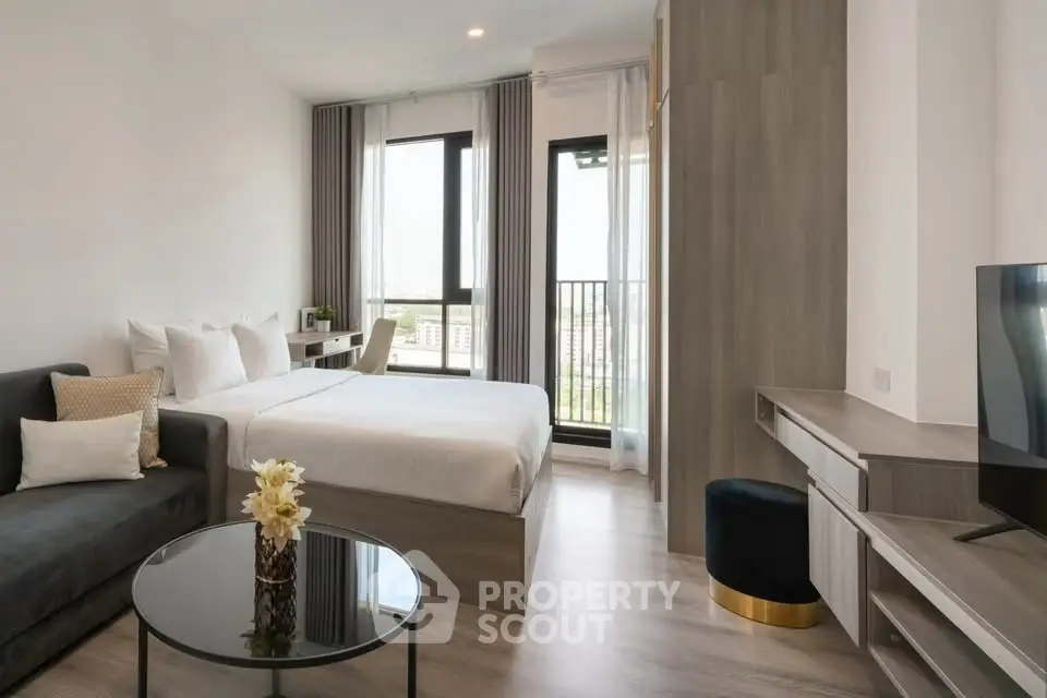 Modern studio apartment with cozy bed, stylish sofa, and city view balcony.