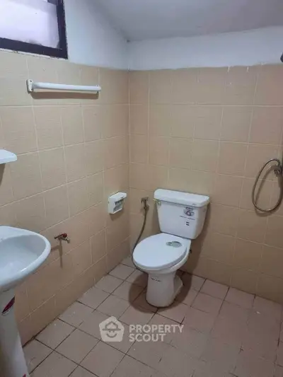Compact bathroom with beige tiles, featuring a toilet, sink, and showerhead.