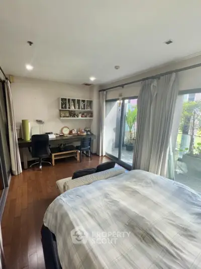 Spacious bedroom with garden view and study area, featuring large windows and wooden flooring.