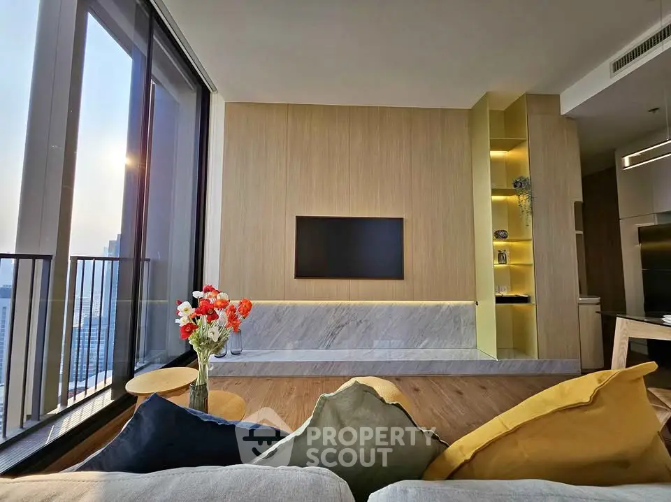 Modern living room with large windows and stylish decor, featuring a wall-mounted TV and vibrant cushions.