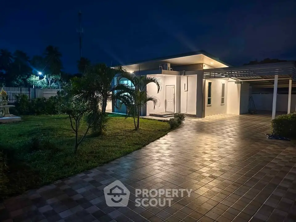 Modern single-story home with spacious driveway and lush garden at night.