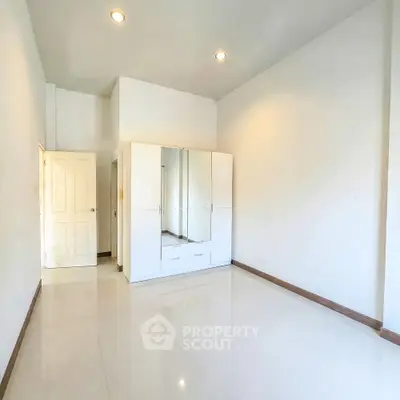 Spacious unfurnished room with sleek white wardrobe and glossy tiled flooring