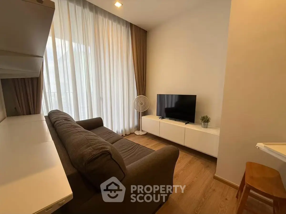 Cozy living room with modern sofa, TV, and floor-to-ceiling windows for natural light.