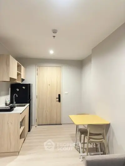 Modern compact kitchen with light wood cabinets and dining area in cozy apartment.