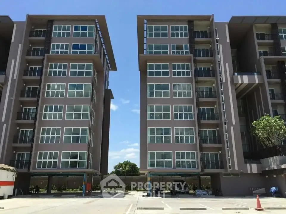 Modern apartment buildings with large windows and open parking area under clear blue sky.