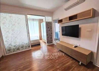 Modern living room with wooden flooring, wall-mounted TV, and sliding doors leading to a bedroom.