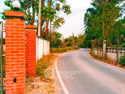 Charming countryside road with lush greenery and red brick entrance, perfect for serene living.