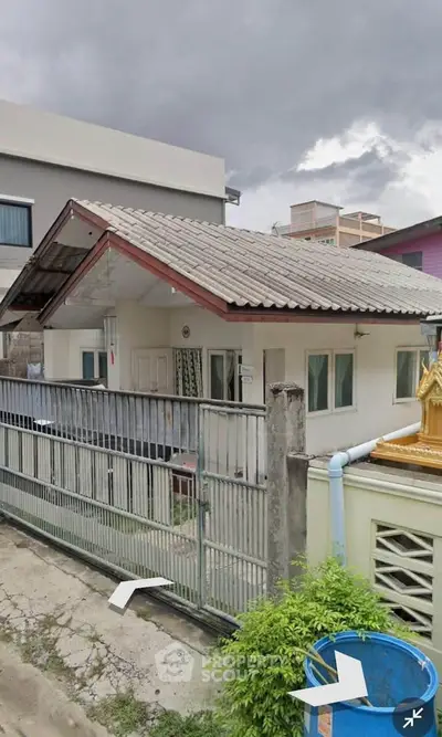 Charming single-story house with sloped roof and gated entrance in a suburban setting.