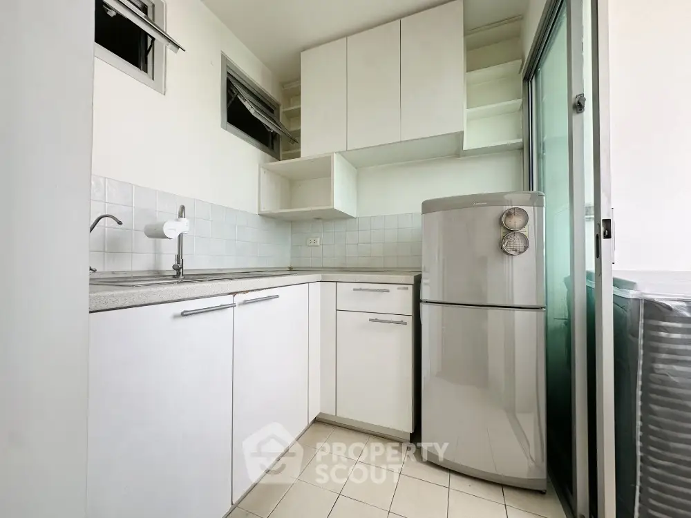 Modern compact kitchen with sleek white cabinets and stainless steel fridge