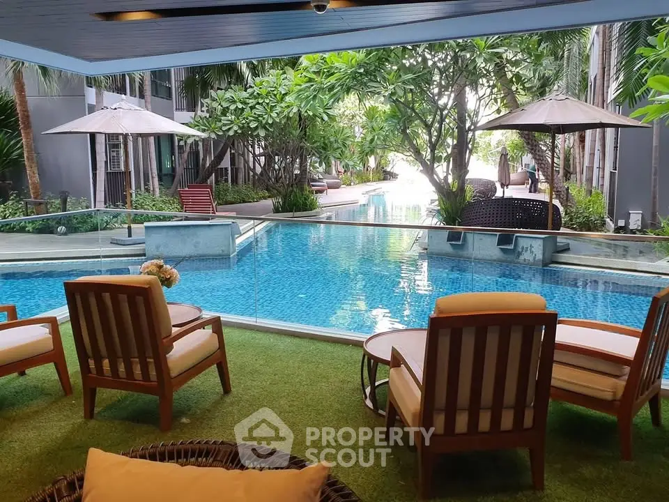 Luxurious poolside view with elegant seating and lush greenery in a modern residential complex.