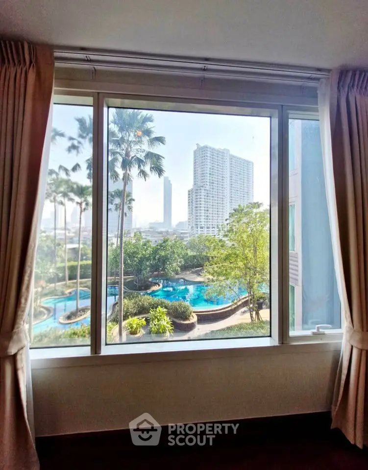 Stunning cityscape view from a window overlooking lush greenery and a sparkling pool.