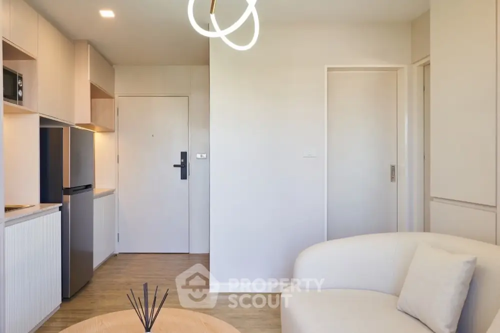 Modern living room with minimalist design, featuring a cozy white sofa and sleek kitchen area with built-in appliances.