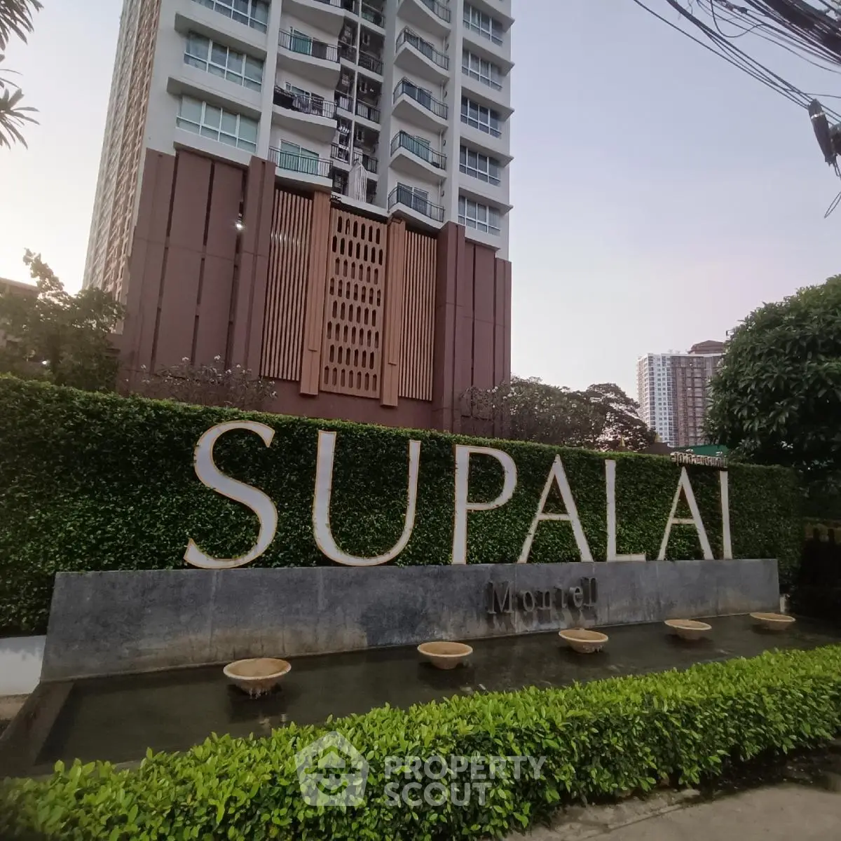 Modern high-rise building exterior with lush greenery and water feature at Supalai Monuel.
