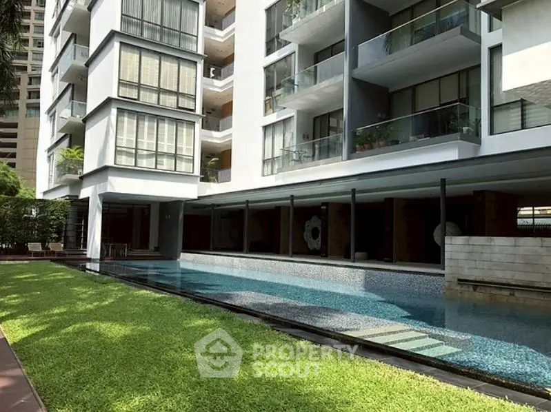 Luxurious modern apartment building with poolside view and lush greenery.