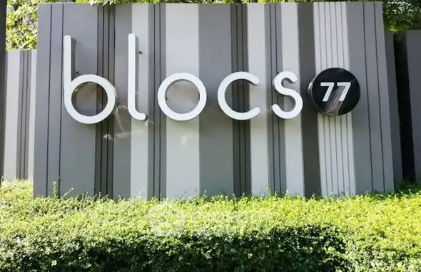 Modern real estate sign for Blocs 77 with sleek design and lush greenery.