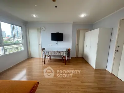 Bright living room with wooden flooring and city view, featuring a wall-mounted TV and dining area.
