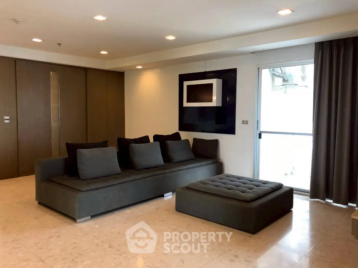 Spacious modern living room with elegant dark sofa and large window for natural light.