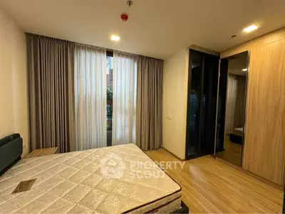 Spacious bedroom with large window and wooden flooring in modern apartment.