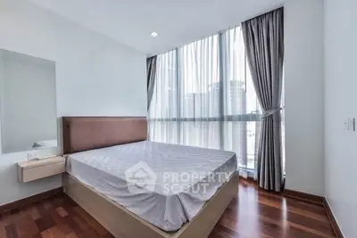Modern bedroom with large windows and city view, featuring hardwood floors and elegant curtains.