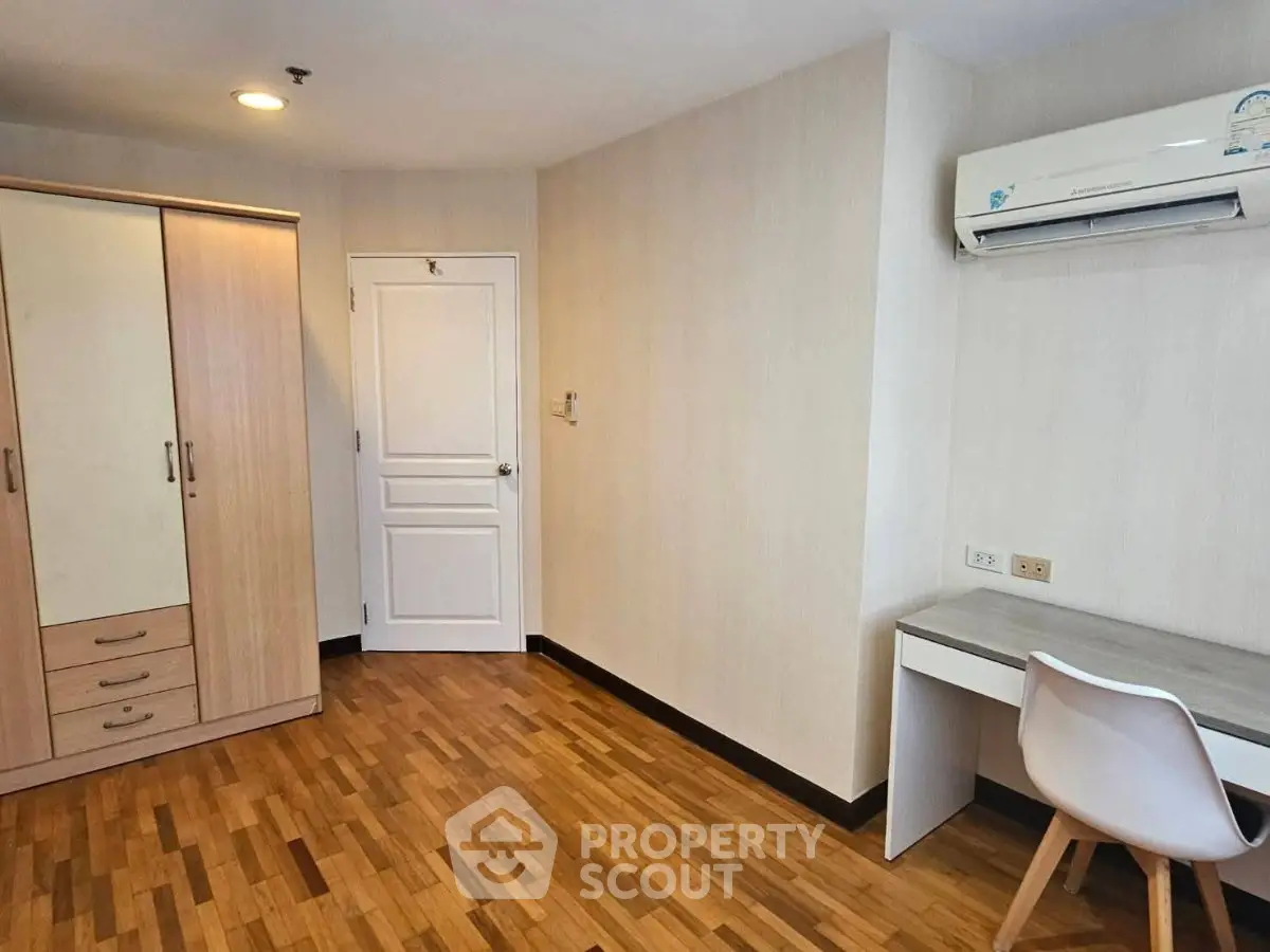 Modern bedroom with wooden flooring, wardrobe, desk, and air conditioning unit.