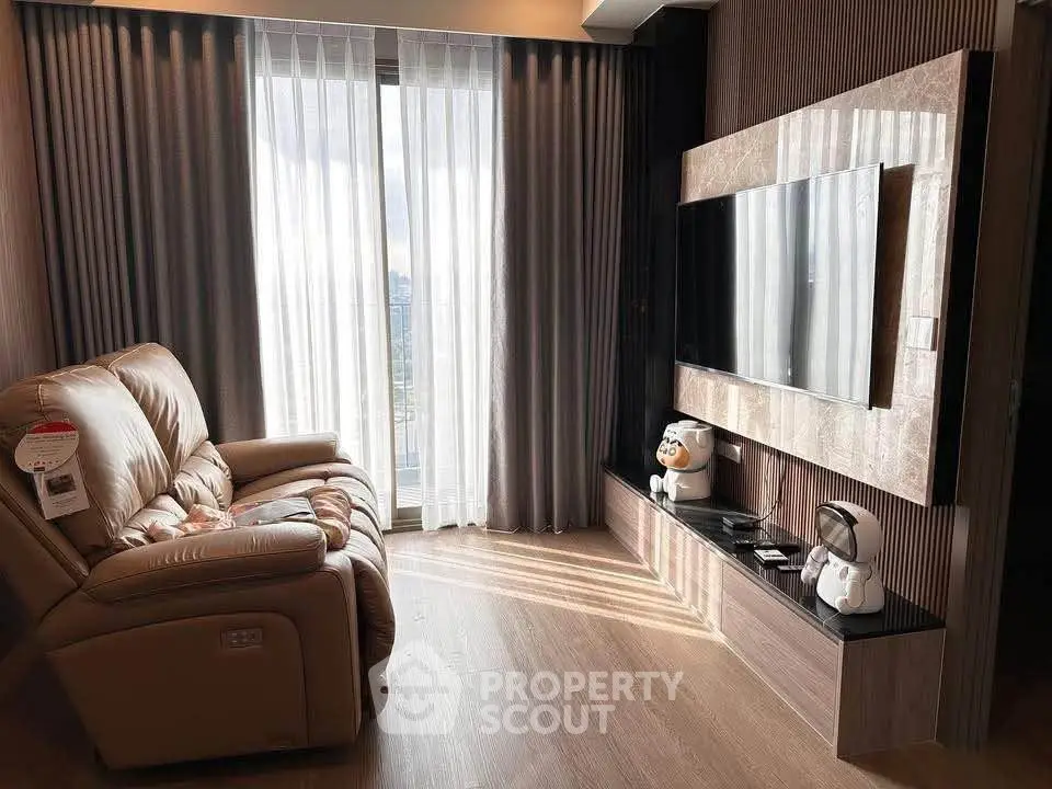 Modern living room with large TV and comfortable recliner, featuring floor-to-ceiling windows and elegant decor.