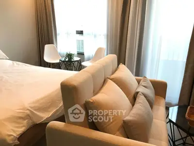 Cozy bedroom with stylish beige sofa and modern chairs by a window, offering a serene and inviting atmosphere.