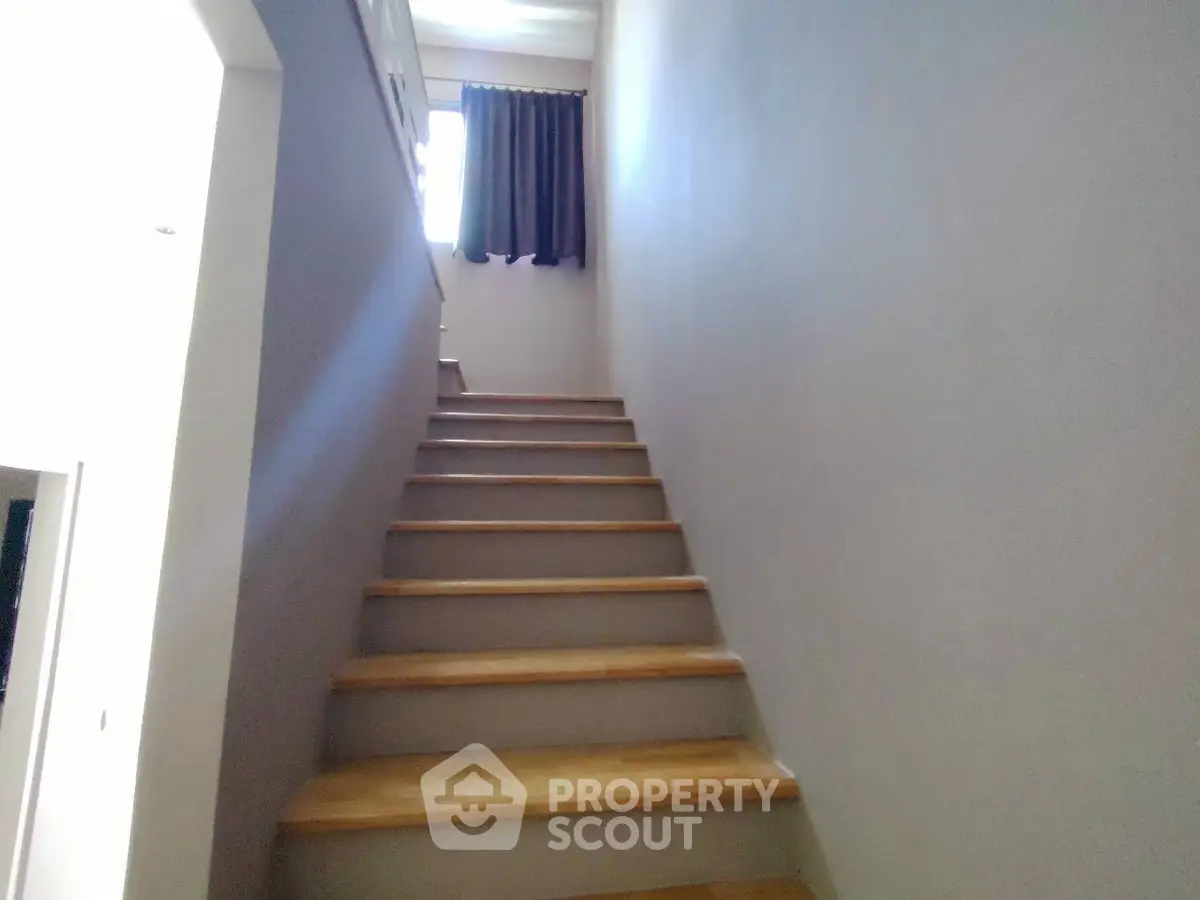 Bright staircase with wooden steps leading to upper floor, featuring a window with curtains.