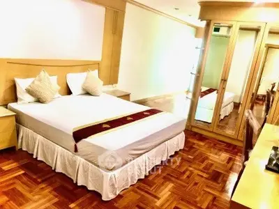 Spacious bedroom with wooden flooring and mirrored wardrobe in modern apartment.