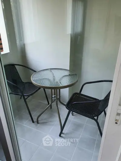 Cozy small balcony with glass table and two chairs, perfect for morning coffee.
