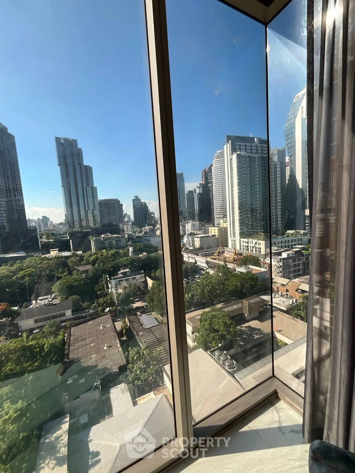 Stunning cityscape view from a high-rise apartment window, showcasing urban skyline and greenery.