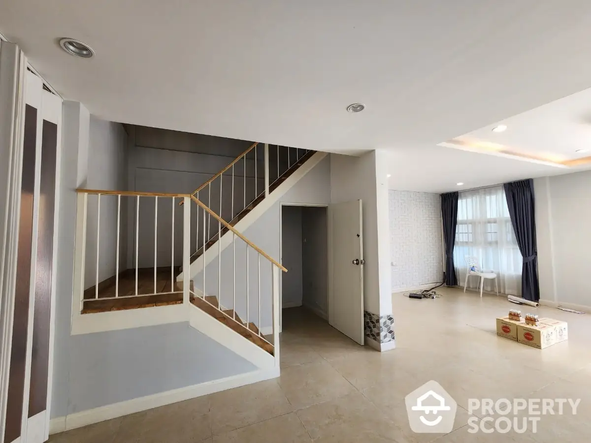 Spacious and modern living area with elegant staircase, sleek tiled flooring, and abundant natural light, perfect for family gatherings and entertaining guests.