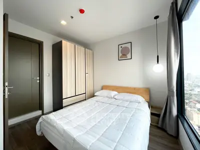 Modern bedroom with city view, featuring minimalist decor and ample natural light.