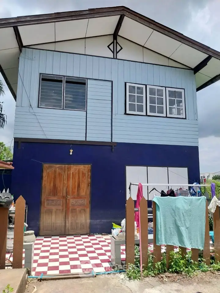Charming two-story blue house with checkered patio and wooden doors, perfect for family living.