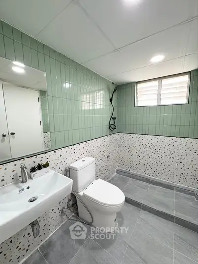 Modern bathroom with stylish green tiles and terrazzo wall, featuring a sleek sink and toilet.