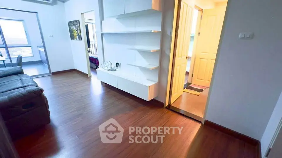 Spacious modern living room with wooden flooring and built-in shelves, leading to a bright balcony view.