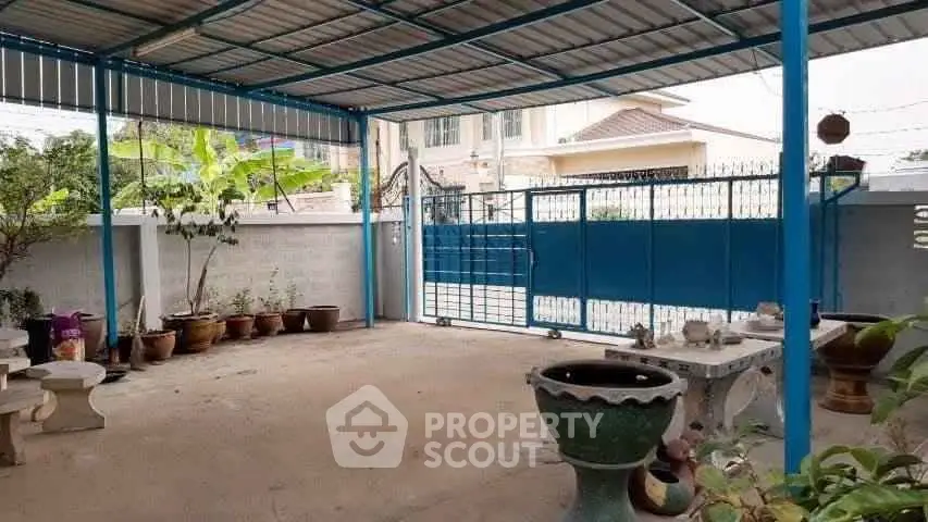 Spacious covered parking area with blue gate and garden pots, ideal for secure vehicle storage.