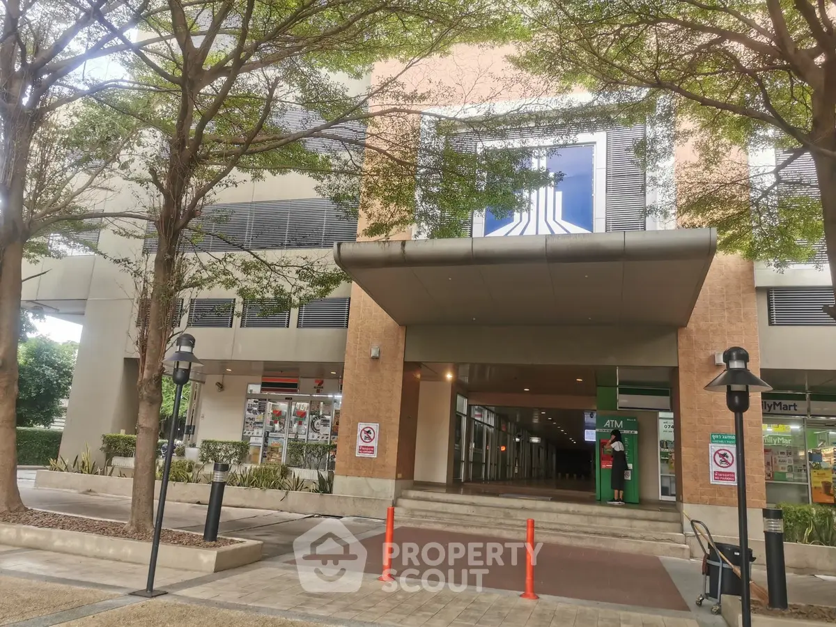 Modern commercial building entrance with lush trees and retail shops