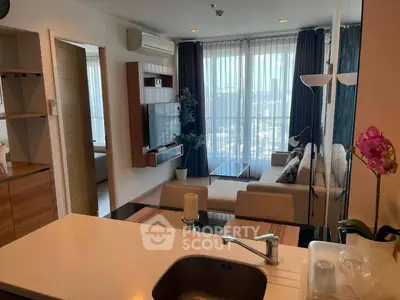 Modern living room with open kitchen, featuring stylish decor and natural light from large windows.