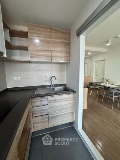 Modern kitchen with sleek wooden cabinets and open layout leading to dining area.
