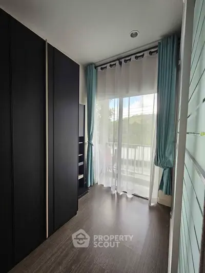 Bright room with large window and modern wardrobe, featuring elegant curtains and wooden flooring.