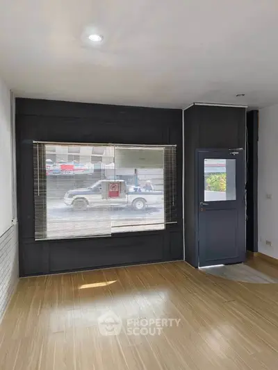 Spacious room with large window and wooden flooring, ideal for versatile use.