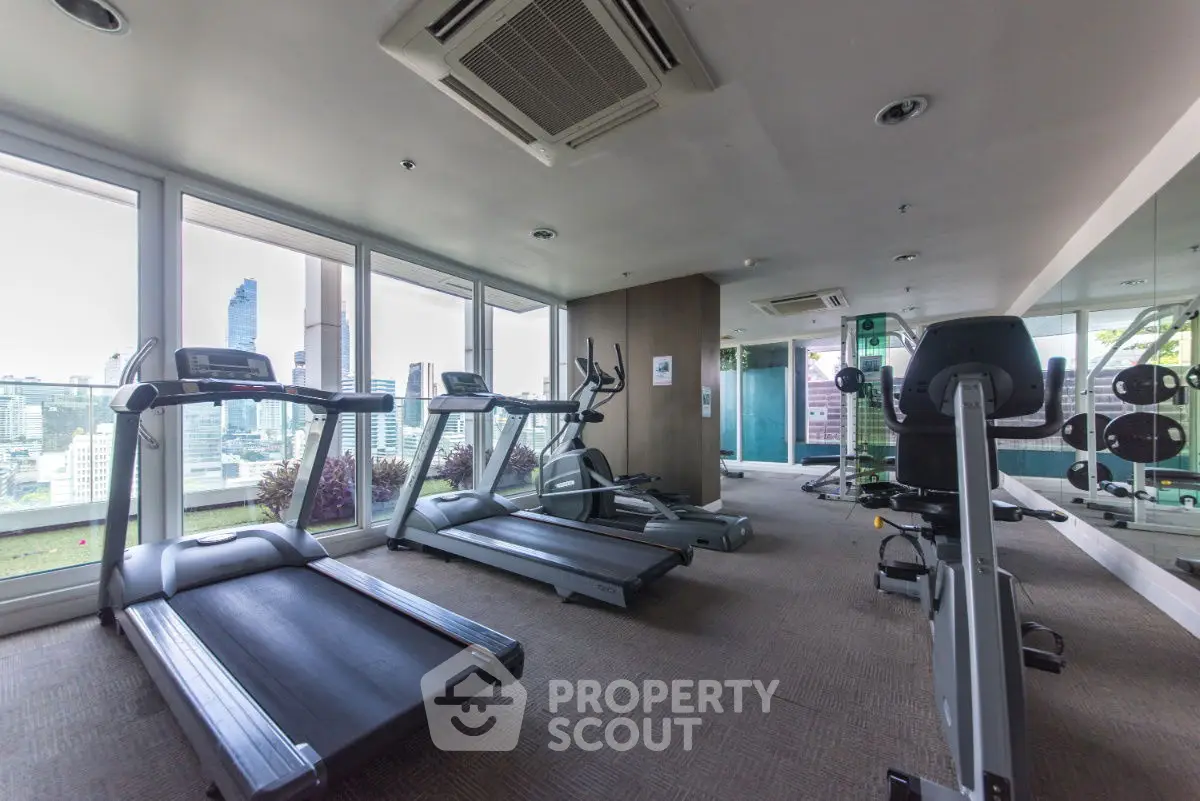 Modern gym with city view, featuring treadmills and exercise equipment in a high-rise building.