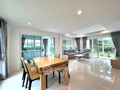 Spacious living room with modern dining area and large windows offering garden views.