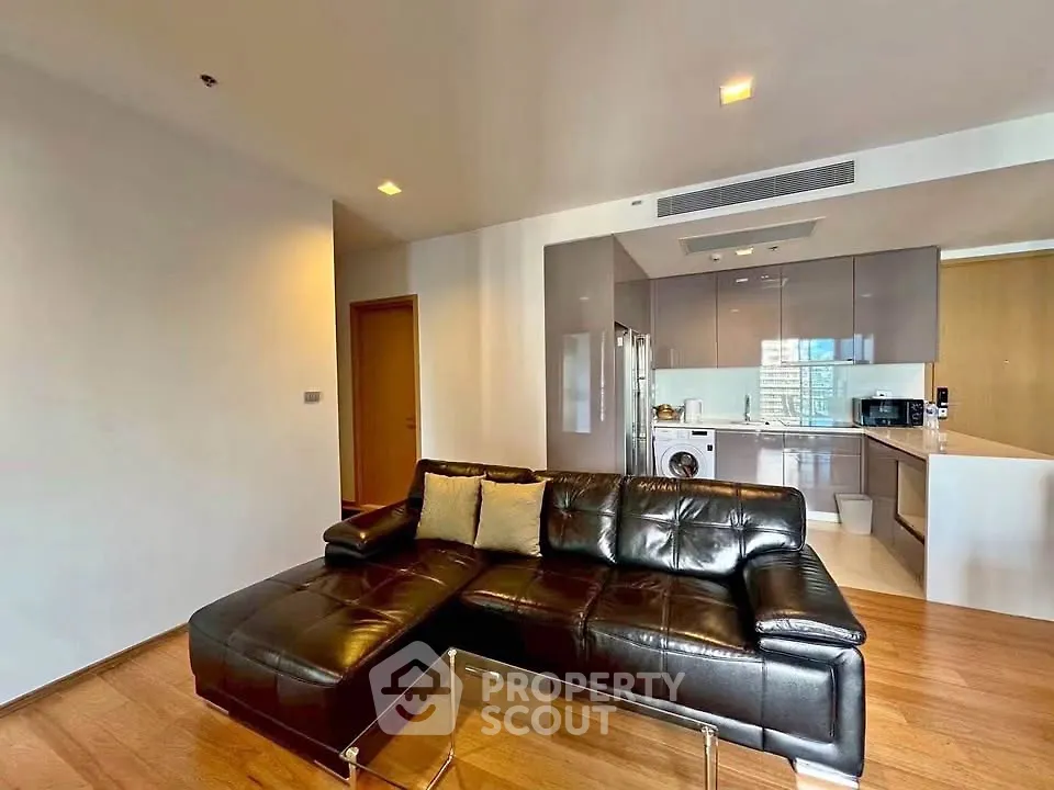 Modern open-layout living room with sleek leather sofa and integrated kitchen featuring stainless steel appliances.