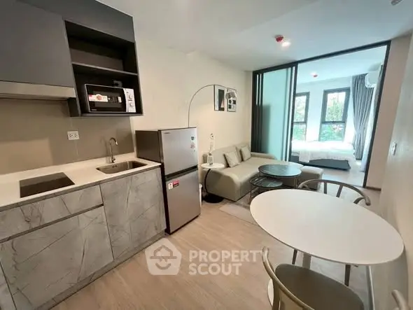 Modern open-plan studio apartment with sleek kitchen and cozy living area, featuring large windows for natural light.