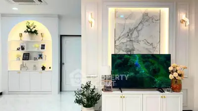 Elegant living room with marble accents and modern decor, featuring built-in shelves and a flat-screen TV.