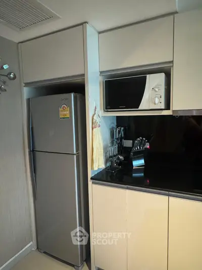 Modern kitchen with stainless steel fridge and microwave, sleek cabinetry, and black countertop.
