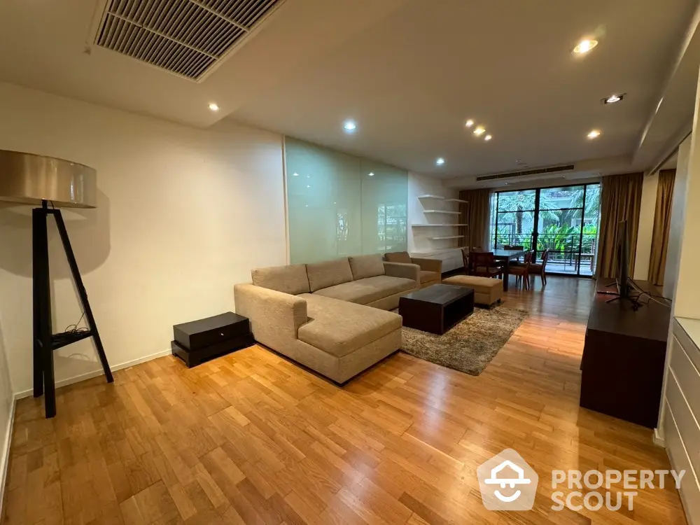 Spacious modern living room with hardwood floors and large windows overlooking greenery.