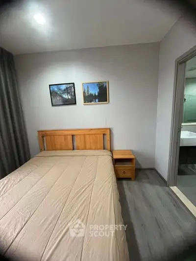 Cozy bedroom with wooden bed frame and nightstand, modern decor, and adjacent bathroom view.